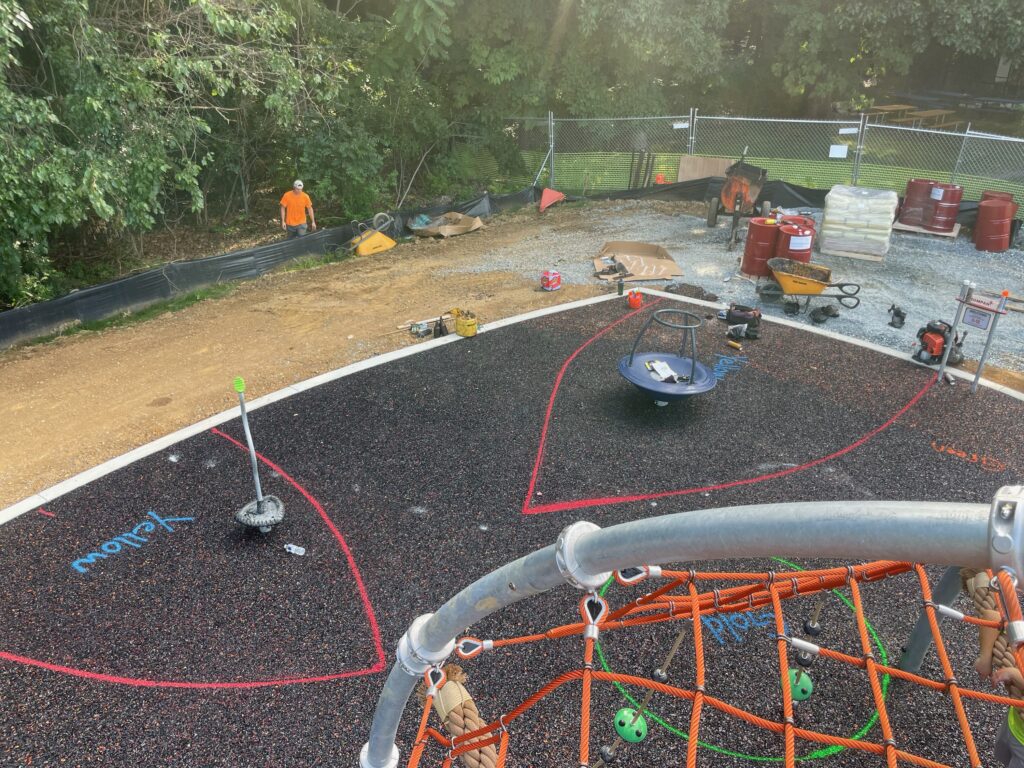 This is a photo view from the climbing structure showing the paint markings for the smaller color poured rubber areas on top of the base rubber layer at the Anne Beers Elementary School playground in Washington, D.C.