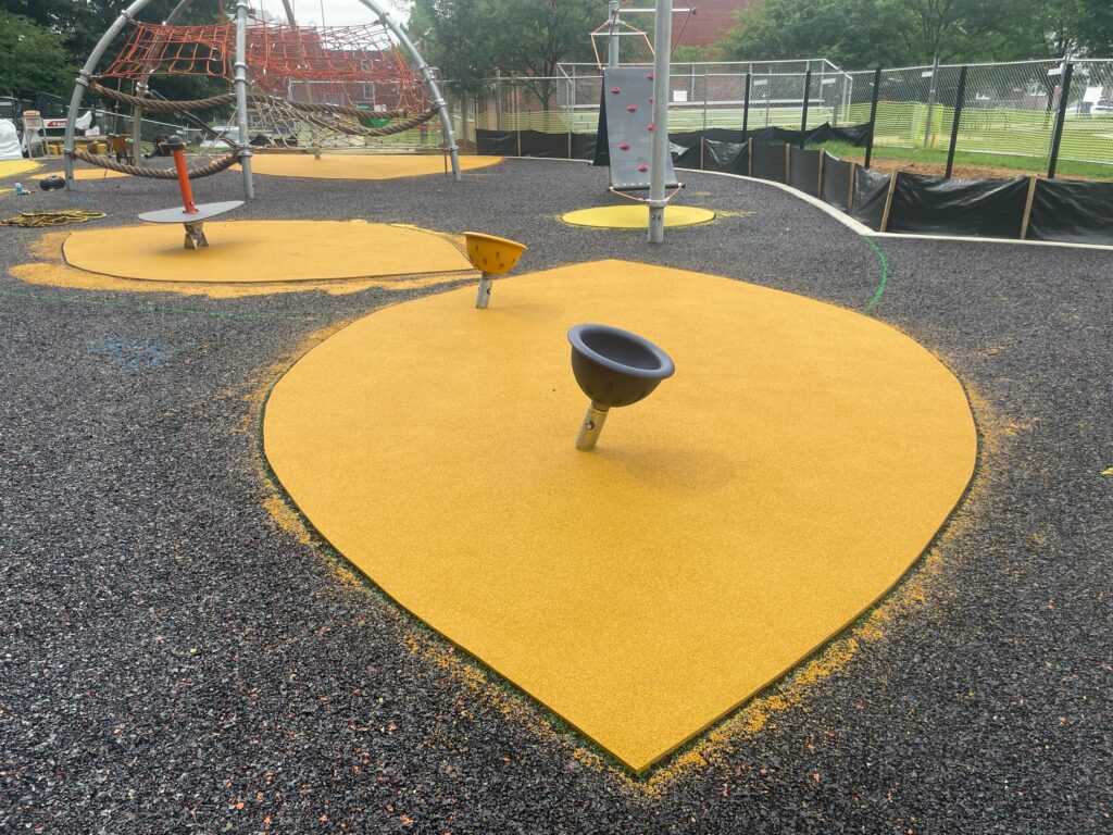 Photo of the smaller poured rubber colored areas from the in front of the climbing structure. This is after the rubber base has been installed but before the final, larger colored rubber area is installed at the Anne Beers Elementary School playground in Washington, D.C.