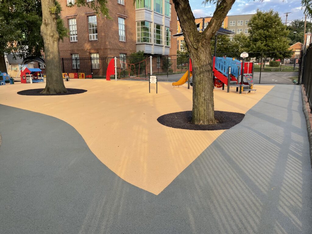 Savoy Elementary School - Custom Park Surfacing - poured rubber and flexi-pave-003 - Custom Park Surfacing Savoy Elementary School - Custom Park Surfacing - poured rubber and flexi-pave-larger view of two trees with root systems protected by flexi-pave as well as the climbing structure behind the trees