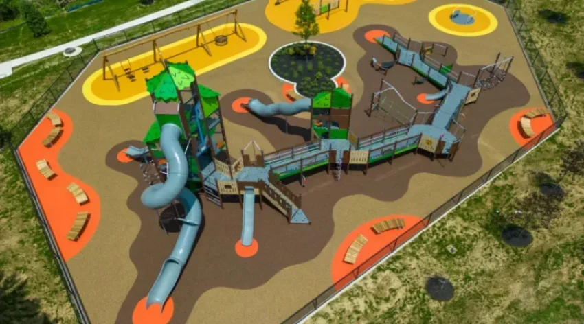Aerial view of a large colorful playground with interconnected slides, bridges, and climbing structures on a brown and orange safety surface.